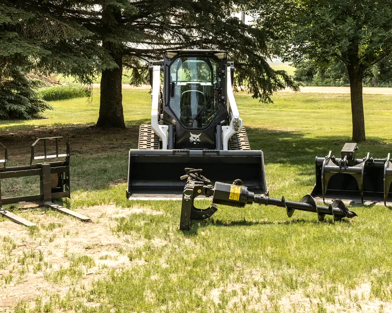 Bobcat compact track loader beside a lineup of Bobcat attachments
