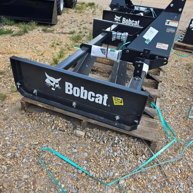 Bobcat box blade attachment with the Bobcat wordmark across the blade, on a pallet on the lot at Dykes Motors in Collins, Mississippi