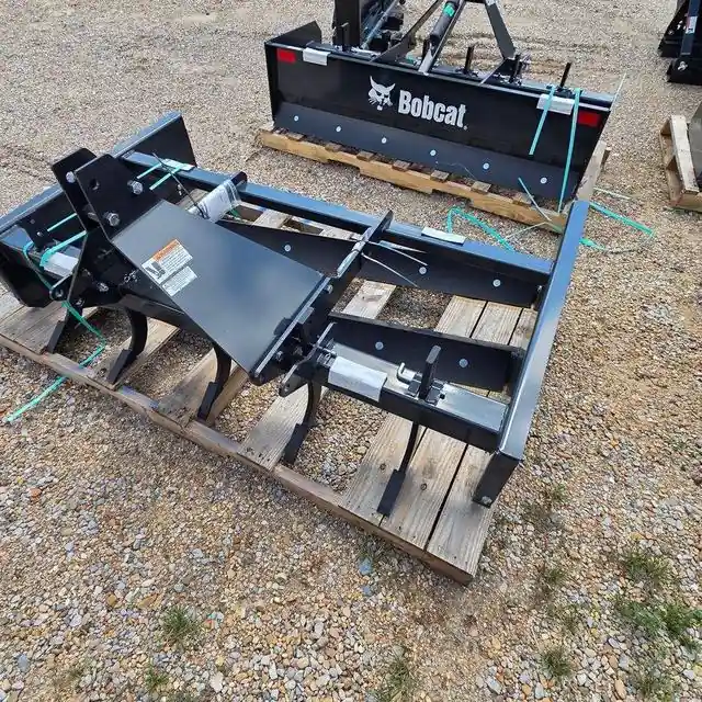Two Bobcat box blades on pallets, one showing its rear ripper shanks and the other the Bobcat wordmark, on the lot at Dykes Motors in Collins, Mississippi