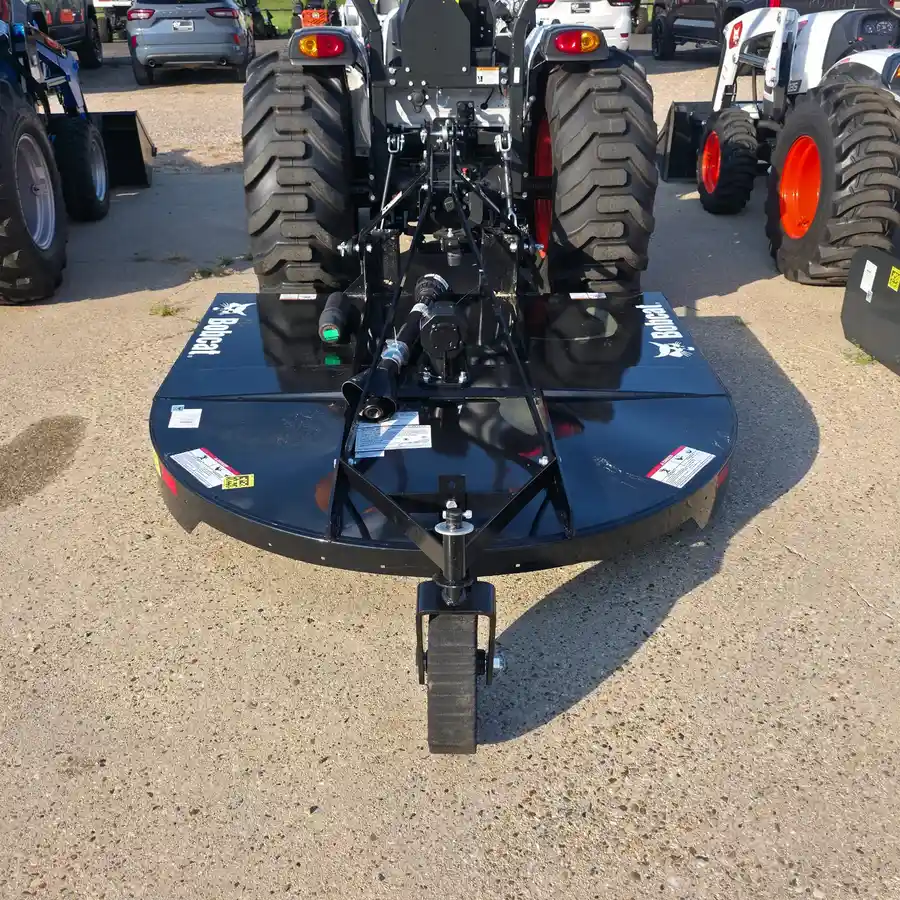 Bobcat rotary cutter attachment, rear view showing the Bobcat wordmark twice on the deck, hitched to a Bobcat compact tractor on the lot at Dykes Motors in Collins, Mississippi