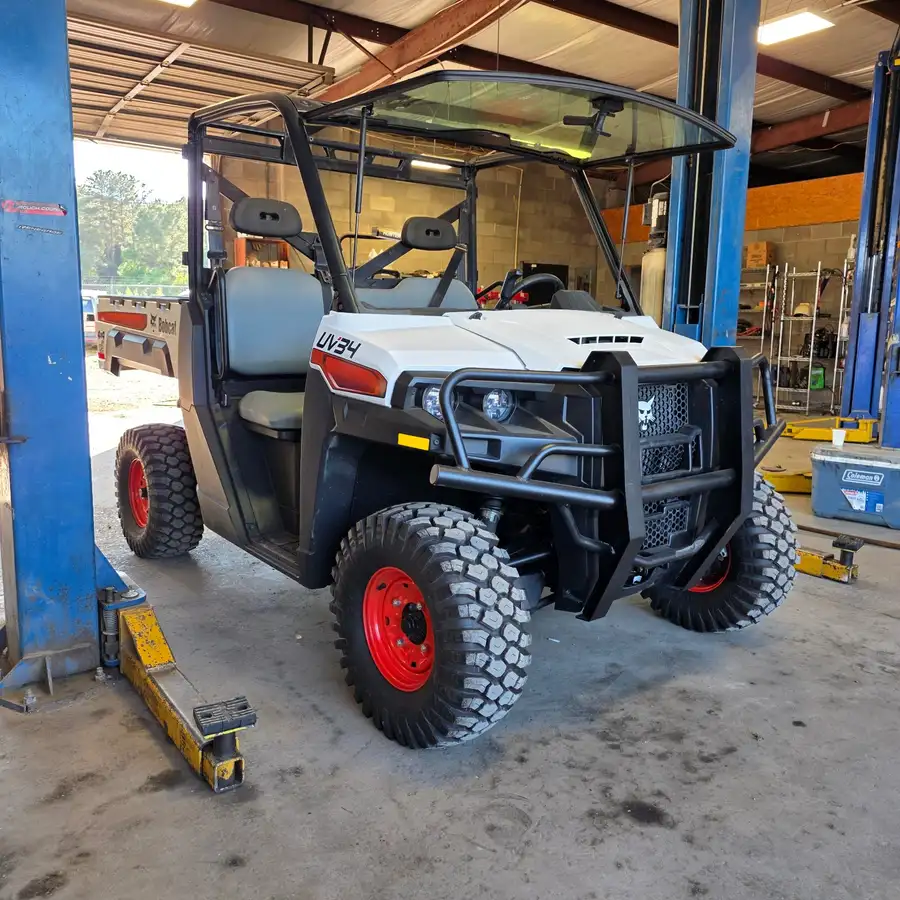 Front three-quarter view of a Bobcat UV34 4x4 EFI utility vehicle on the shop lift at Dykes Motors, dealer-installed front brush guard fitted