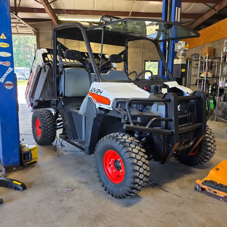 Front three-quarter view of a Bobcat UV34 4x4 EFI utility vehicle on the shop lift at Dykes Motors, cargo bed tilted up