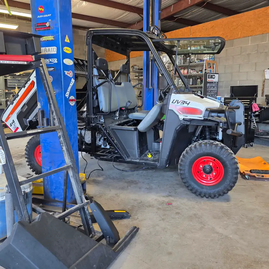 Driver side profile of a Bobcat UV34 4x4 EFI utility vehicle on the shop lift at Dykes Motors, cargo bed tilted up