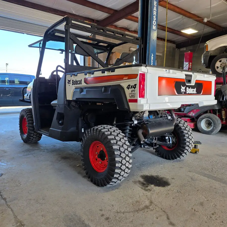 Rear three-quarter view of a Bobcat UV34 4x4 EFI utility vehicle on the shop lift at Dykes Motors, red steel wheels and cargo rack visible