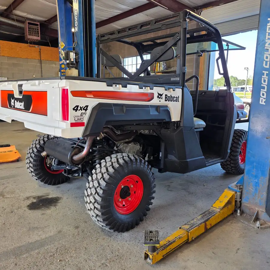 Rear three-quarter view of a Bobcat UV34 4x4 EFI utility vehicle on the shop lift at Dykes Motors, opposite side, door open