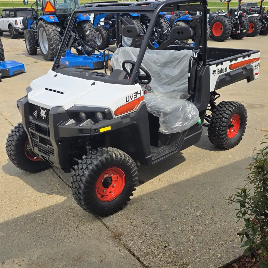 Rear three-quarter view of the new Bobcat UV34 4x4 diesel showing the cargo box with the Bobcat 4x4 diesel badge, LS tractors and implements in the background