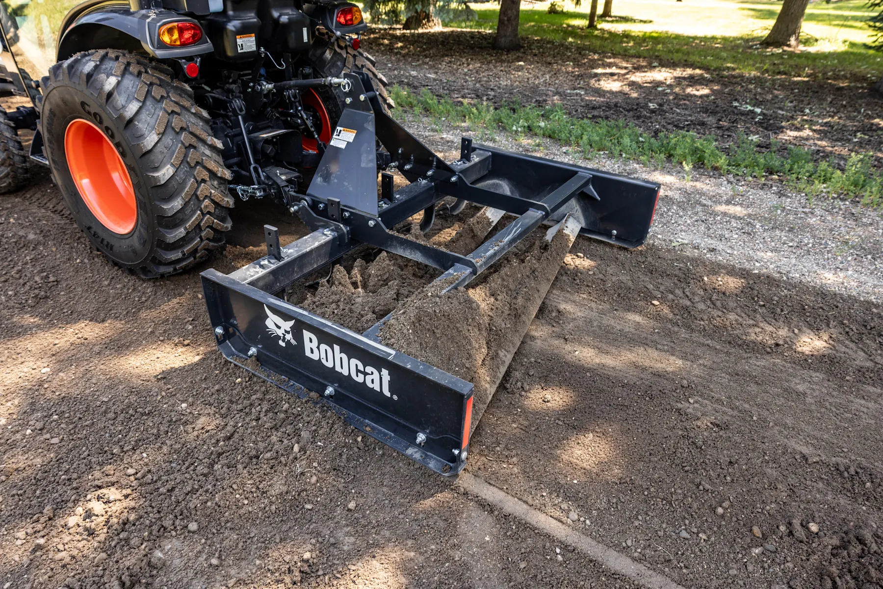 Bobcat 3-point land grader attachment leveling soil behind a compact tractor